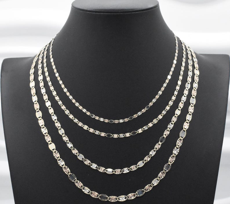 Puede incluir: Un conjunto de cinco collares plateados expuestos sobre un maniqu&iacute; negro. Cada collar presenta una delicada cadena con eslabones ovalados y en forma de estrella. Los collares var&iacute;an en longitud, creando un efecto de capas.