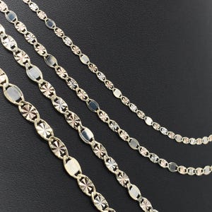 Puede incluir: Cuatro delicados collares de oro con diferentes dise&ntilde;os de cadena. Las cadenas presentan eslabones ovalados y en forma de estrella, creando un efecto brillante. Los collares se exhiben sobre un fondo oscuro.