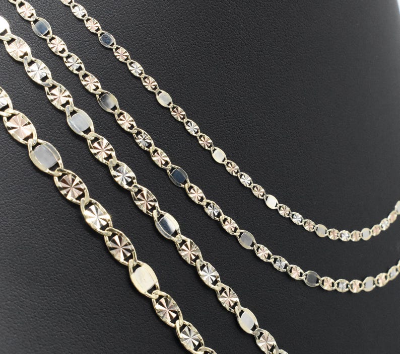 Puede incluir: Cuatro delicados collares de oro con diferentes dise&ntilde;os de cadena. Las cadenas presentan eslabones ovalados y en forma de estrella, creando un efecto brillante. Los collares se exhiben sobre un fondo oscuro.