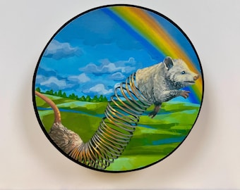 May include: A circular painting featuring a white opossum with a long, flexible metal spring for a body. The background depicts a vibrant green landscape under a blue sky with white clouds and a colorful rainbow arching across the top of the scene.