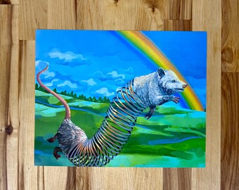 May include: A rectangular art print featuring a surreal illustration of a grey opossum with a long, metallic, coiled spring body. The creature is set against a vibrant landscape of green rolling hills, a bright blue sky, and a colorful rainbow.