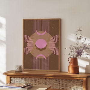 Op de afbeelding: Een ingelijste kunstdruk met een geometrisch ontwerp in bruine en roze tinten. Het kunstwerk bevat een centrale roze cirkel, halve maanvormen en gebogen lijnen. De print wordt getoond op een houten tafel met een vaas bloemen.