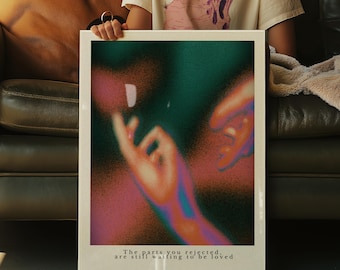 May include: A framed art print with a surreal, abstract design. The artwork features a blend of green, pink, and orange hues, with a blurred depiction of hands. The text at the bottom reads, "The parts you rejected, are still waiting to be loved."