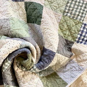 May include: A patchwork quilt in shades of blue, green, and cream. The quilt features a variety of patterns, including stripes, checks, and solid squares. The quilt is quilted with a diamond pattern and has a soft, textured appearance.