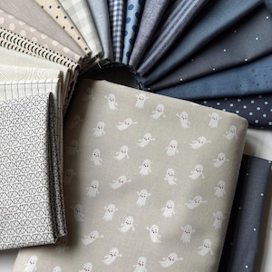 May include: A collection of folded fabric squares arranged in a fan shape. The fabrics feature various patterns including white ghosts on a beige background, black geometric lines, polka dots, stripes, and solid shades of blue, gray, and cream.