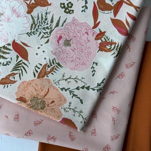 May include: Three fabric swatches in shades of cream, pink, and rust. The top swatch features a floral pattern with pink peonies, rust-colored leaves, and green ferns. The middle swatch is a solid pink with small floral accents. The bottom swatch is a solid rust color.