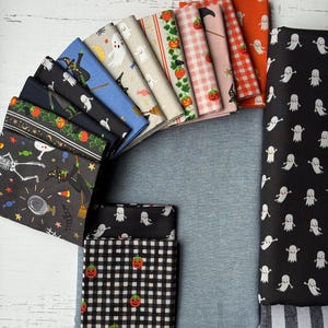 May include: A collection of folded fabric squares featuring various Halloween-themed patterns including ghosts, pumpkins, witches, skeletons, and candy. The fabrics display a range of colors such as black, orange, blue, pink, and white in plaid and print designs.