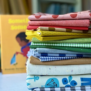 May include: A tall stack of folded fabric pieces in various colors and patterns, including red polka dots, solid red, yellow geometric prints, green solids, green gingham, blue stripes, blue gingham, tan, speckled cream, and blue floral prints.
