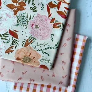 May include: Four fabric swatches in shades of pink and white. The top swatch features a floral pattern with large pink and peach flowers, and brown and green leaves. The second swatch is solid pink with small floral accents. The third is a pink and white gingham.