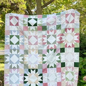 May include: A patchwork quilt with a variety of colors and patterns, including green, pink, white, and blue. The quilt is made up of squares with different designs, including stars, diamonds, and gingham.