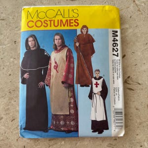 May include: A McCall's Costumes sewing pattern envelope M4627 featuring illustrations of four different historical-style robes. The designs include a black hooded robe, a red and gold patterned tunic, a brown monk-style habit, and a white tabard with a red cross.