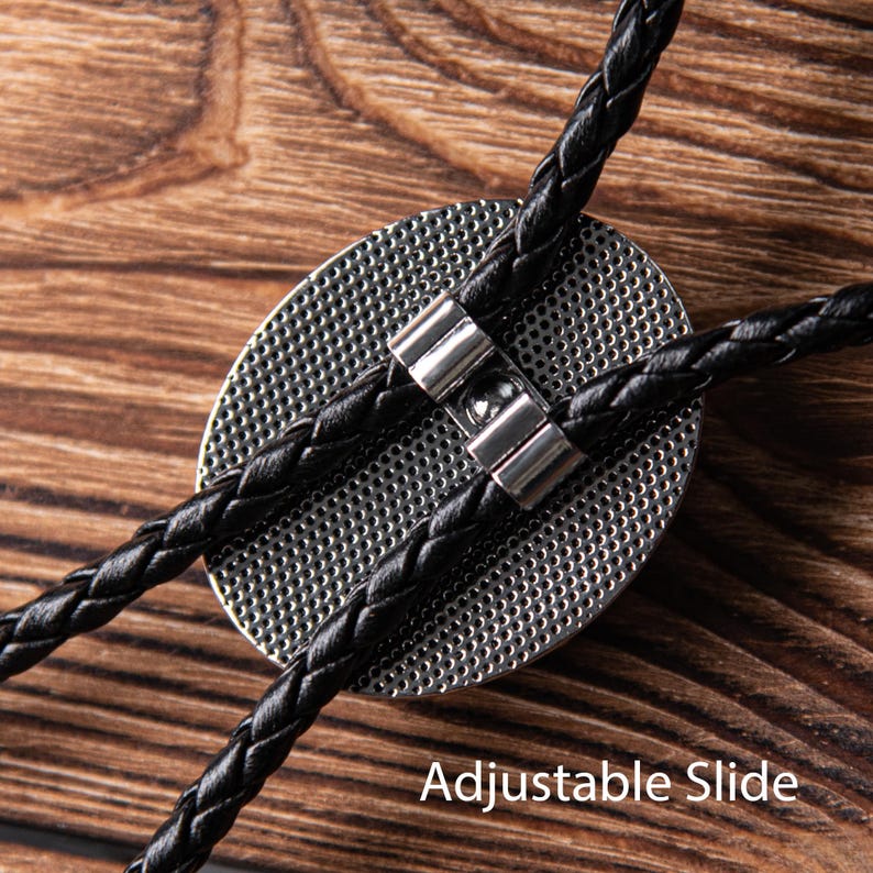 May include: A black bolo tie with an adjustable slide. The tie has a braided leather cord and a round metal pendant.