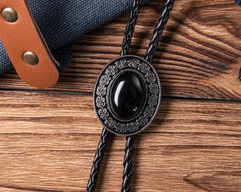May include: A black bolo tie with a silver oval pendant featuring a black gemstone. The pendant has an intricate design around the gemstone.