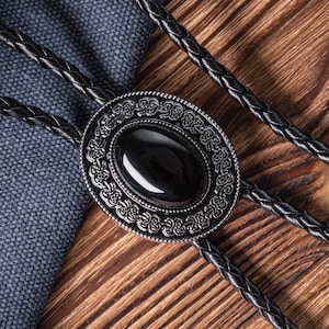 May include: A black bolo tie with a silver oval pendant featuring an intricate design and a black stone in the center.