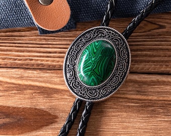 May include: Oval bolo tie with a silver-toned filigree border and a green malachite stone center. The tie features a black braided leather cord and a brown leather strap with a metal button.