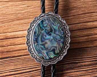 May include: Oval bolo tie with a silver-colored filigree frame. The center features a polished abalone shell with iridescent blue, green, and silver tones. The braided black leather cord completes the design.