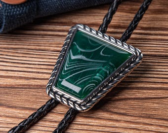 May include: A green and silver bolo tie with a braided black leather cord. The tie features a green stone with white swirls set in a silver frame.