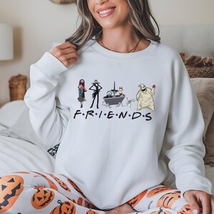 A woman wearing a white sweatshirt with a graphic design featuring characters from the TV show Friends.