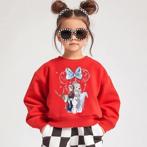 A young girl wearing a red sweater with a cartoon character design, sunglasses, and checkered pants.