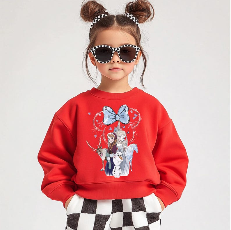 A young girl wearing a red sweater with a cartoon character design, sunglasses, and checkered pants.