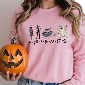 A woman wearing a pink sweater with a graphic of characters from the TV show Friends holding a carved pumpkin.