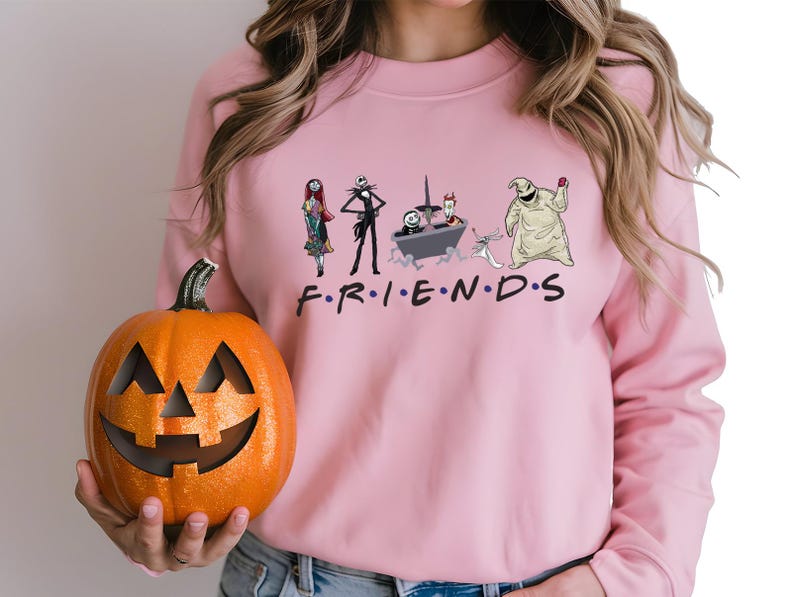 A woman wearing a pink sweater with a graphic of characters from the TV show Friends holding a carved pumpkin.
