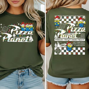A woman wearing a green t-shirt with a design featuring characters from the animated film "Pizza Planet".