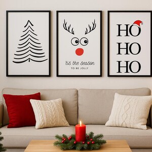 Peut inclure: Trois impressions d'art de Noël encadrées avec des cadres noirs sont accrochées au-dessus d'un canapé beige. Les impressions présentent un sapin de Noël minimaliste, un visage de renne et le texte "Ho Ho Ho". Un sapin de Noël décoré et une couronne sont également visibles.