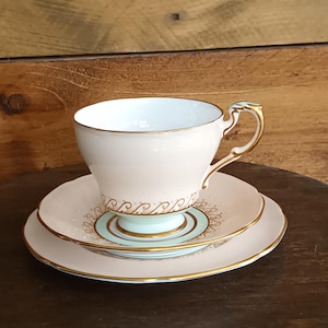 Puede incluir: Un juego de taza y platillo de té rosa con ribete dorado y un delicado patrón floral. La taza y el platillo están hechos de porcelana fina y tienen un aspecto vintage.