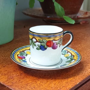 Peut inclure: Une tasse à thé et une soucoupe blanches avec un motif floral jaune, bleu et vert orné de baies rouges, violettes et bleues.