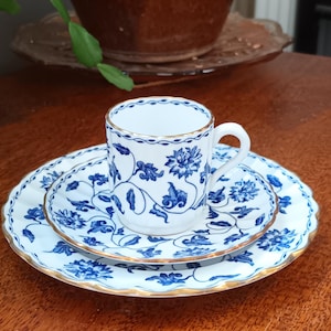 May include: A white porcelain teacup and saucer set with a blue and gold floral pattern. The cup has a gold rim and the saucer has a scalloped edge.