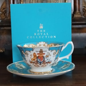 Może przedstawiać: Zestaw do herbaty z cienkiej porcelany z filiżanką i spodkiem w kolorze turkusowym i złotym. Filiżanka ma białe wnętrze i uchwyt. Zestaw pochodzi z The Royal Collection.