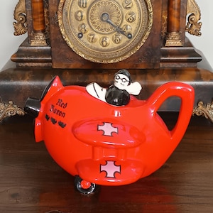 Könnte beinhalten: Eine weiße Keramik-Tasse mit schwarzem Henkel und dem Text "But First, Coffee" in schwarzer, handschriftlicher Schrift. Die Tasse steht auf einer weißen Oberfläche.