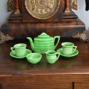 Może przedstawiać: Jasnozielony ceramiczny zestaw do herbaty składający się z czajnika z pokrywką, dwóch filiżanek z pasującymi spodkami, małego dzbanuszka na śmietankę oraz małej miseczki. Każdy element posiada wyraźną poziomą prążkowaną fakturę na powierzchni.