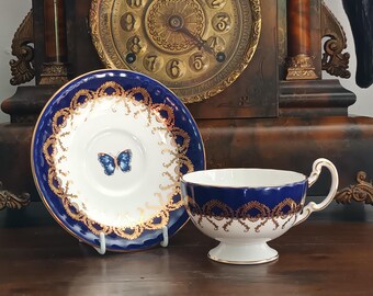 Fabulosa y rara taza y platillo vintage de porcelana fina inglesa Aynsley azul y dorado con diseño de mariposas y flores campestres, de la década de 1950, en excelente estado.