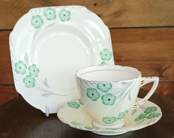 Precioso y raro juego de té Art Decó Grafton "Fantasía" de porcelana inglesa Bone China. Taza, platillo y plato de té con trébol verde dorado, década de 1930. En perfecto estado.