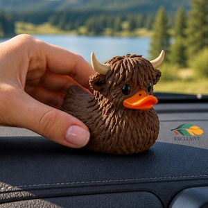 May include: A brown rubber duck toy featuring a textured, shaggy coat, two small cream-colored horns, and a bright orange beak. The duck has dark, round eyes and is designed with a shaggy, fur-like appearance, combining the features of a duck and a highland cow.