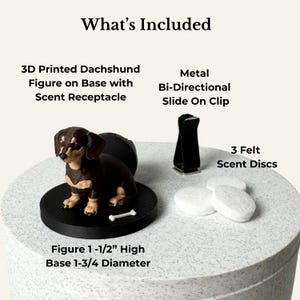 May include: A 3D printed brown and black dachshund figure on a black circular base with a scent receptacle, a metal bi-directional slide-on clip, and three white felt scent discs. The figure is 1-1/2 inches high and the base is 1-3/4 inches in diameter.