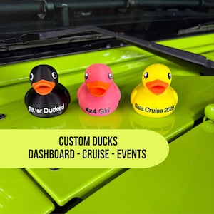 May include: Three rubber ducks in black, pink, and yellow with orange beaks and white eyes. The black duck says "Git'er Ducked", the pink duck says "4x4 Girl", and the yellow duck says "Gals Cruise 2025". The image also includes the text "CUSTOM DUCKS DASHBOARD - CRUISE - EVENTS".