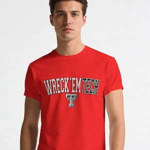 May include: A bright red short-sleeved crew neck t-shirt featuring the text WRECK 'EM TECH in a white and black arched collegiate font, with a stylized letter T logo positioned directly below the text in matching white and black colors.