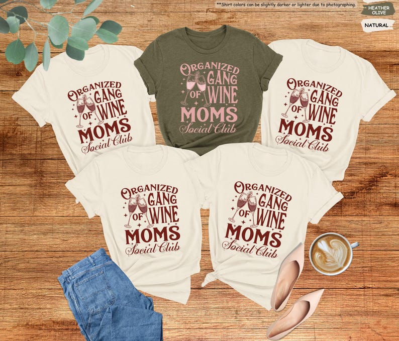 May include: Five t-shirts with the text "ORGANIZED GANG OF WINE MOMS Social Club" in a burgundy color. One shirt is olive green, and the others are natural. A pair of blue jeans, shoes, and a cup of coffee are also in the image.
