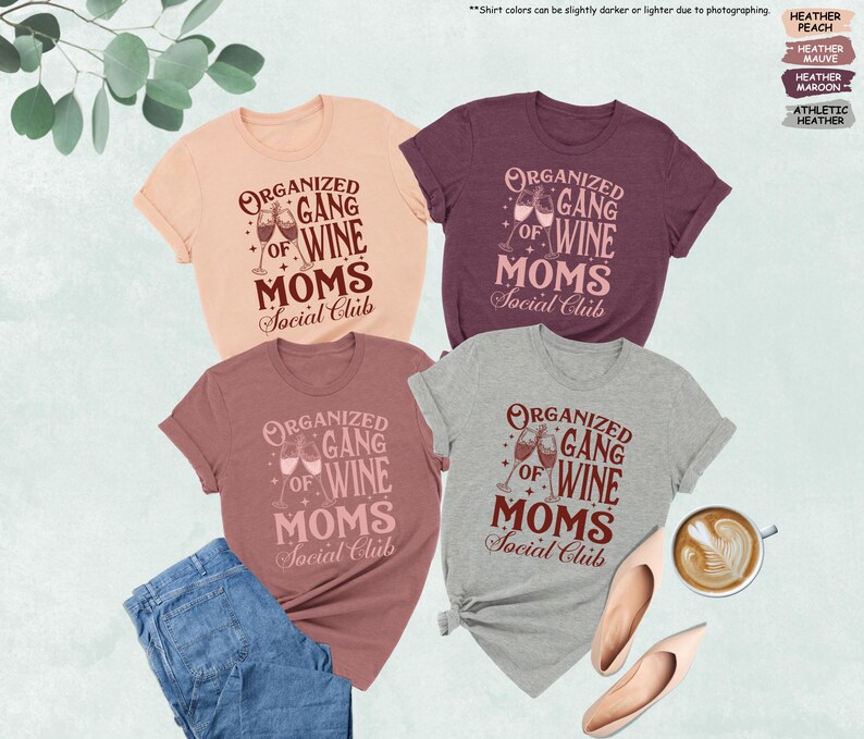 May include: Four t-shirts in peach, maroon, mauve, and athletic heather colors, each with the text "Organized Gang of Wine Moms Social Club" in a decorative font. The design includes wine glasses. A pair of jeans, shoes, and a cup of coffee are also in the image.