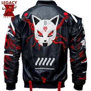 Puede incluir: Chaqueta bomber de cuero negro con bordados rojos y blancos. La chaqueta presenta una máscara de zorro blanca con ojos rojos y un diseño rojo y blanco en las mangas. La chaqueta tiene una cremallera y un cuello de canalé.