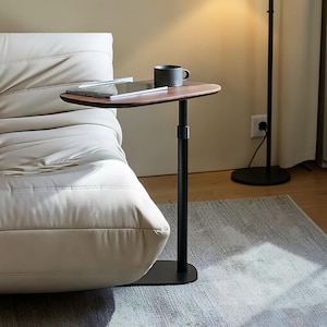 May include: A modern side table with a dark wood-grain top and a black metal base. A black mug and a tablet rest on the table. The table is next to a white sofa.
