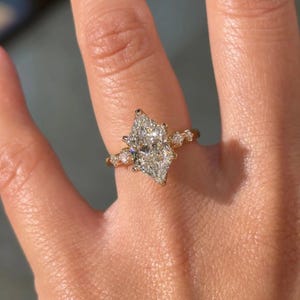 May include: A gold ring featuring a large marquise-cut center stone and two smaller round-cut accent stones on each side. The band is crafted from polished yellow gold, providing a warm metallic contrast to the clear, faceted stones set in prongs.