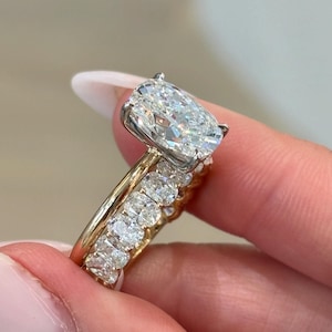 May include: A two-piece ring set featuring a large oval-cut centre stone in a silver-toned prong setting on a gold band, paired with a matching eternity band encrusted with smaller oval-cut stones set in a continuous gold metal channel.
