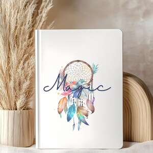 Könnte beinhalten: Weißes Notizbuch mit einem Aquarell-Traumfänger-Design. Der Traumfänger zeigt ein gewebtes Netz, Federn und das Wort "Magic" in Schreibschrift. Das Design enthält Farbtöne von Blau, Orange und Lila.