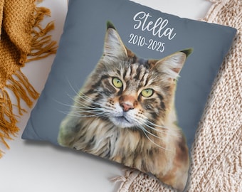 May include: A square decorative pillow featuring a detailed portrait of a Maine Coon cat with green eyes and long whiskers. The cat's name, "Stella", and the years "2010-2025" are printed in white script on the pillow. The pillow has a blue-gray background.