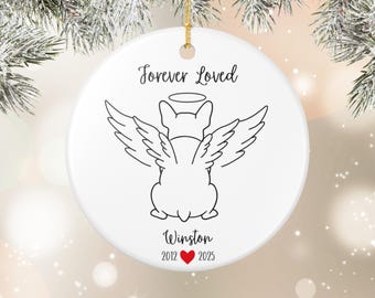 May include: White ceramic Christmas ornament with a gold string for hanging. The ornament features a black line drawing of a dog with angel wings and a halo. Text reads "Forever Loved" and "Winston" with dates 2012 and 2025.