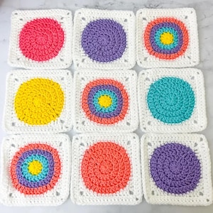 Könnte beinhalten: Neun gehäkelte Quadrate mit weißen Rändern und farbenfrohen kreisförmigen Designs. Die Kreise weisen Farbtöne von Rosa, Lila, Orange, Gelb und Türkis auf. Die Quadrate sind in einem Raster von drei mal drei angeordnet.
